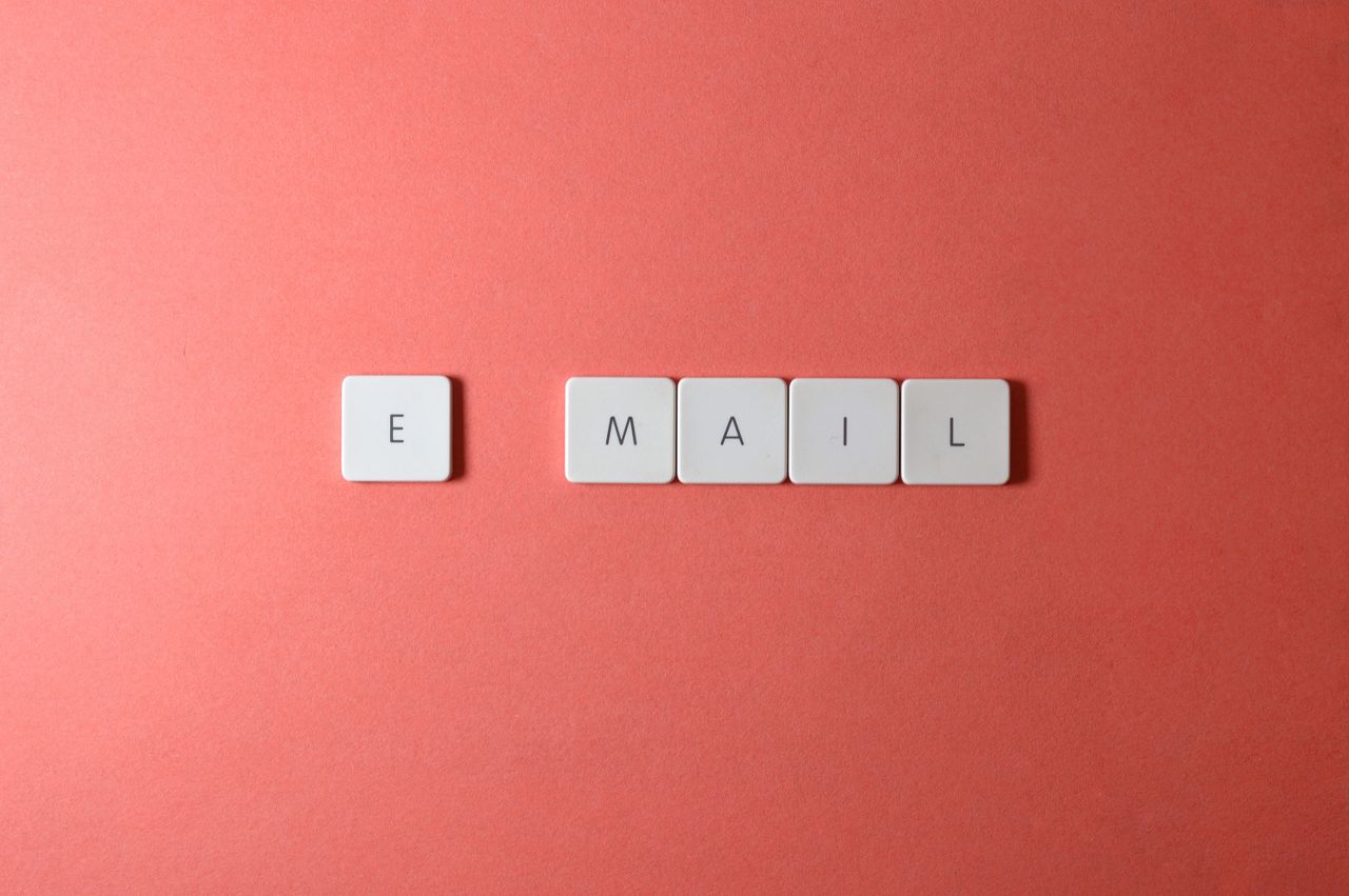 heros-img Flat lay of keyboard letter tiles spelling email on coral backdrop.
